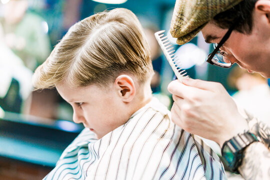 A barber holds a comb doing haircut for a boy.