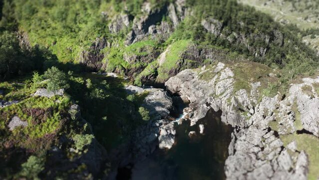 An aerial view of the waterfall on the river in the rocky valley. Tilt-shift video, slow-motion.