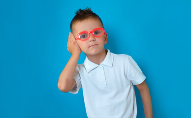 Funny boy with glasses holds his hand near his ear and listens attentively. Interesting news in...