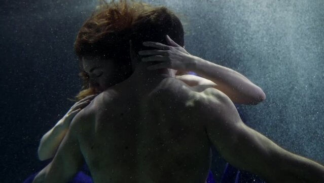 a man with a naked torso is visible from the back. a woman hugs a male head, then strokes shoulders in dark water with bubbles
