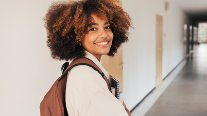 Fototapeta Smiling girl looking back while walking in high school corridor obraz