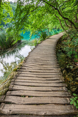 Fototapeta na wymiar Plitvice, Croatia - Wooden walkway in Plitvice Lakes National Park on a bright summer day with crystal clear turquoise water, small waterfalls and green summer foliage