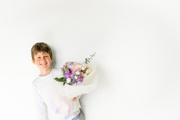 Portrait of a smiling eight-year-old Caucasian boy with a bouquet of flowers in his hands.  A greeting card layout with a place to copy