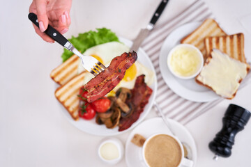 Fried eggs, bacon, tomato, toasted bread in white ceramic plate and cup of coffee