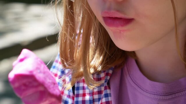 close-up. a little blonde girl eats pink ice cream in the park.
