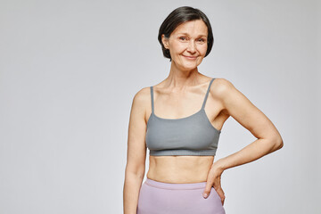 Minimal waist up portrait of smiling mature woman wearing neutral underwear against grey...