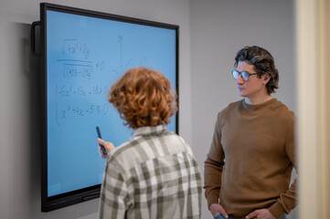 Ginger boy writing on the board, teacher standing next to him