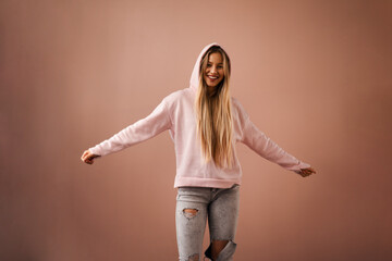 Fashion studio portrait of a happy young blonde woman in hoodie posing over pink background.