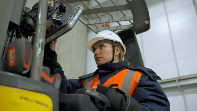 Woman in white helmet sits in forklift truck pressing button on monitor. Female engineer checks operation of equipment in warehouse closeup slow motion