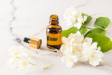 an open bottle of jasmine oil and a dropper with a cosmetic product against fragrant jasmine...