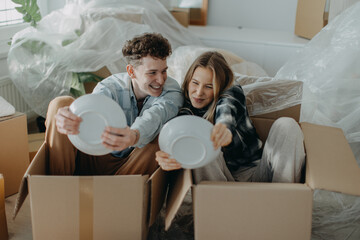 Cheerful young couple in their new apartment, having fun when unpacking. Conception of moving.