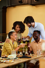 Interracial friends are toasting for success in a restaurant with red wine.