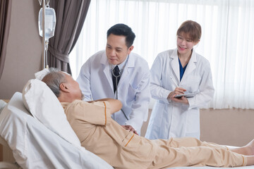 Obraz premium Asian doctor and nurse visit and take care senior man patient in room. Attractive two therapist practitioner explain diagnosis in hospital ward to treatment to elderly older male during appointment.