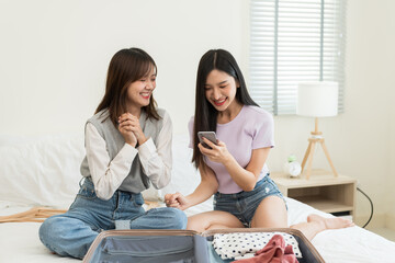 Asian beautiful two women friend use smartphone to look booking hotel. Attractive young female couple traveler feeling happy and enjoy, preparing luggage and ready for holiday vacation trip together. 