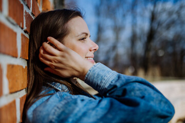 Side view portrait of young woman in denim jacket leaning the brick wall outdoors in summer