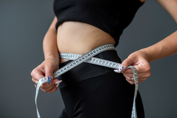 smiling woman measures her ideal waist with a tape measure and shows the result of her diet.