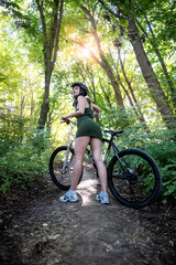 Happy young girl rides a bicycle in the forest on hot summer day