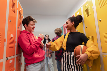 Young high school students meeting and greeting near locker in campus hallway talking and high fiving.