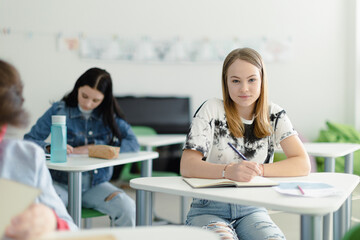 Fototapeta premium High school students paying attention in class, sitting in their desks and writing notes, back to school concept.