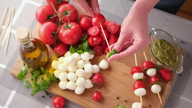 making caprese canapes sticking cherry tomatoes and mozzarella cheese balls on a skewer