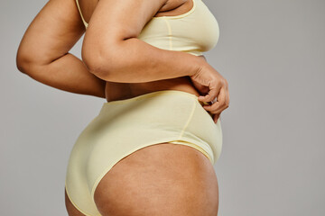 Minimal closeup of unrecognizable black woman wearing underwear against grey background, focus on...