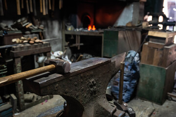 Fototapeta na wymiar Close up view of heated metal and anvil. Blacksmith in the production process of other metal products handmade in the forge. Metalworker forging metal with a hammer into knife. Metal craft industry.