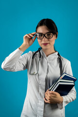 Smiling female doctor with stethoscope and books in hands posing isolated on plain background