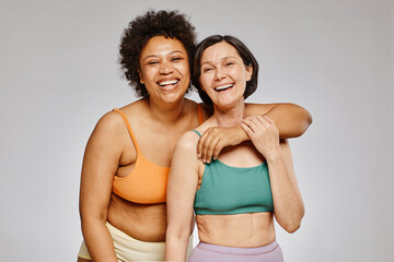 Minimal waist up portrait of two real women wearing underwear and laughing happily against grey...