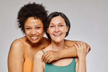 Minimal waist up portrait of two real women embracing and smiling happily against grey background