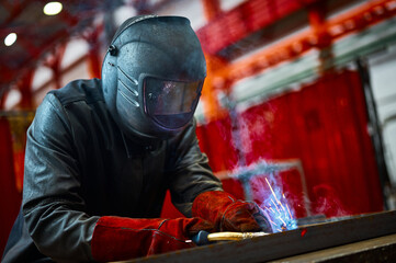 Fototapeta Employee in protective mask and gloves welds metal carcass obraz