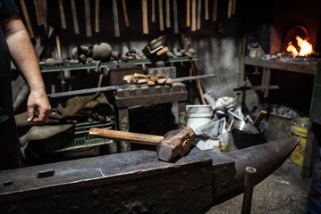 Close up view of heated metal and anvil. Blacksmith in the production process of other metal products handmade in the forge. Metalworker forging metal with a hammer into knife. Metal craft industry.
