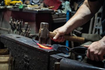 Close up view of heated metal and anvil. Blacksmith in the production process of other metal products handmade in the forge. Metalworker forging metal with a hammer into knife. Metal craft industry.