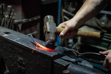 Close up view of heated metal and anvil. Blacksmith in the production process of other metal products handmade in the forge. Metalworker forging metal with a hammer into knife. Metal craft industry.