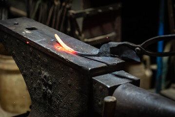 Close up view of heated metal and anvil. Blacksmith in the production process of other metal products handmade in the forge. Metalworker forging metal with a hammer into knife. Metal craft industry.