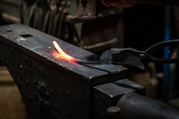 Close up view of heated metal and anvil. Blacksmith in the production process of other metal products handmade in the forge. Metalworker forging metal with a hammer into knife. Metal craft industry.