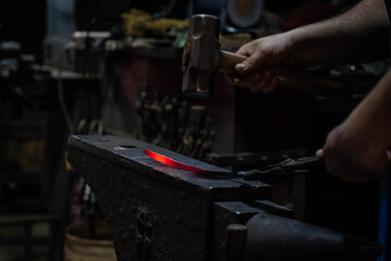 Close up view of heated metal and anvil. Blacksmith in the production process of other metal products handmade in the forge. Metalworker forging metal with a hammer into knife. Metal craft industry.