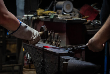 Close up view of heated metal and anvil. Blacksmith in the production process of other metal products handmade in the forge. Metalworker forging metal with a hammer into knife. Metal craft industry.