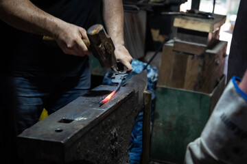 Close up view of heated metal and anvil. Blacksmith in the production process of other metal products handmade in the forge. Metalworker forging metal with a hammer into knife. Metal craft industry.