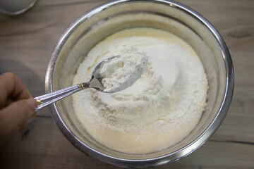 Spoon of flour above bowl with flour and dough. Adding flour to bowl to make dough. Flour for dough preparation for cake and bakery. Step for making muffins, pie, biscuit. Baking process step by step.