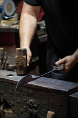 Close up view of heated metal and anvil. Blacksmith in the production process of other metal products handmade in the forge. Metalworker forging metal with a hammer into knife. Metal craft industry.