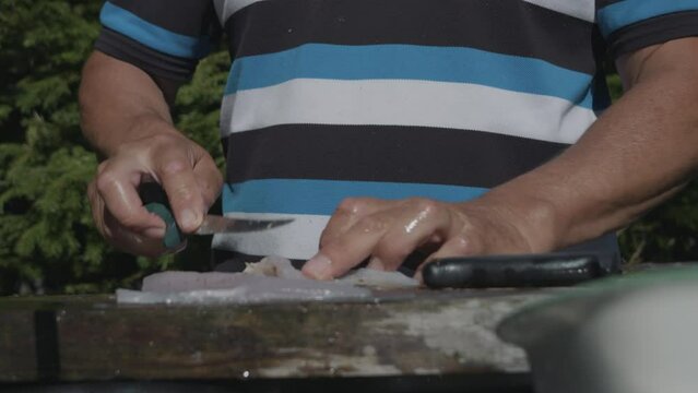 Male hands cleaning fish with sharp knife outdoors in sunny day. Gimbal