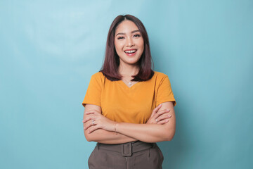 Portrait of a confident smiling girl standing with arms folded and looking at camera isolated over blue background