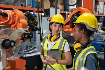 Women Engineer wearing helmet and hi visible vest using laptop computer working in factory welding robotic automation happy smiling with quality control and programming pass 
