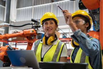 Women Engineer wearing helmet and hi visible vest using laptop computer working in factory welding...