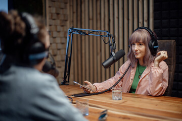 Young woman host talking to microphone and interviewing a man for a radio podcast.