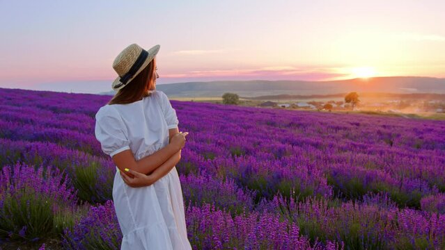 Beautiful young woman wearing white dress and hat standing in a lavender field
