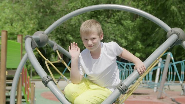 4K. A child on a playground in the park waves at the camera
