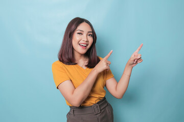 An excited young woman presenting and pointing upwards the copy space, isolated on blue background