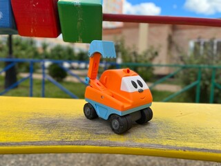Obraz premium Vivid colorful shot of a children's toy excavator on a yellow wooden deck against toy cubes and blurred backdrop. Cute bright toy excavator with eyes, nose and smile