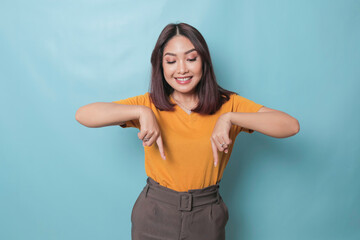 An excited young woman presenting and pointing downwards the copy space, isolated on blue background